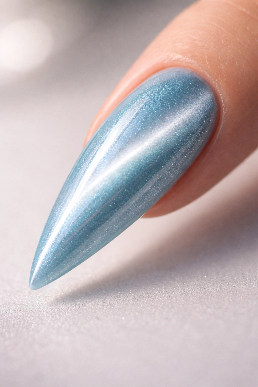 Close-up of a baby blue stiletto nail with a shifting cat eye stripe on a neutral background
