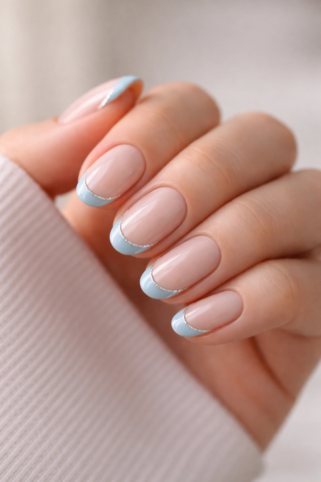 Close-up of short oval nails with baby blue french tips outlined in silver