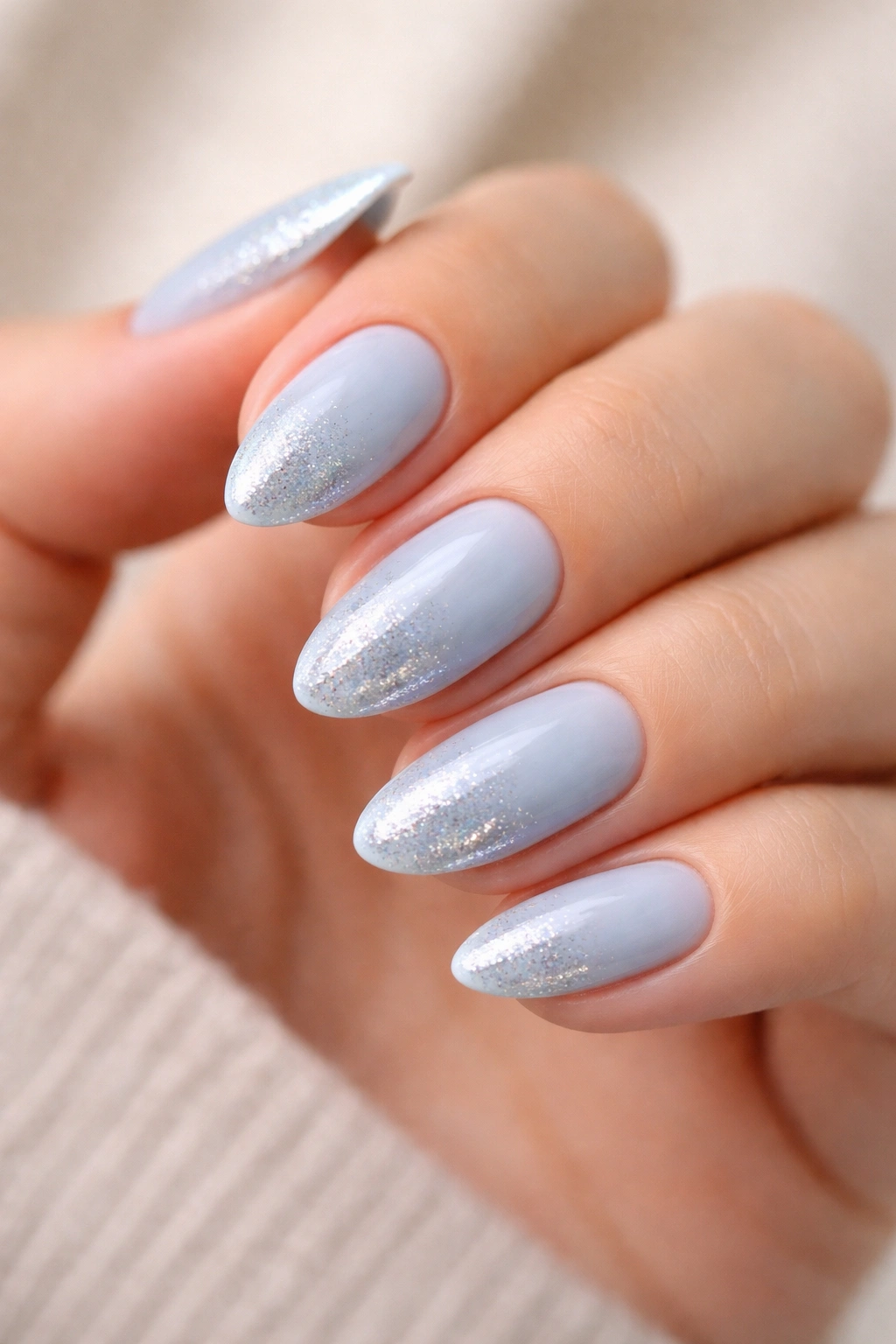 Close-up of short almond nails with baby blue polish and silver glitter fade at the tips.