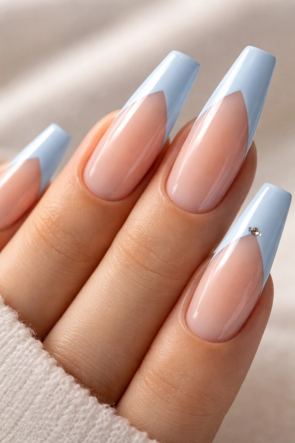 Close-up of a ballerina nail with a diagonal baby blue tip and a small silver stud