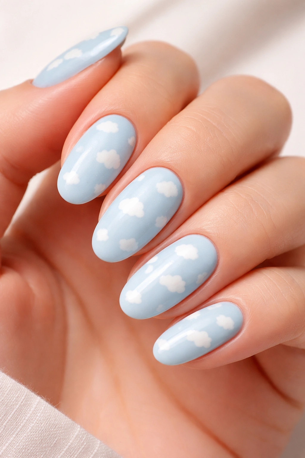 Close-up of baby blue oval nails with tiny white clouds for a soft summer nail design