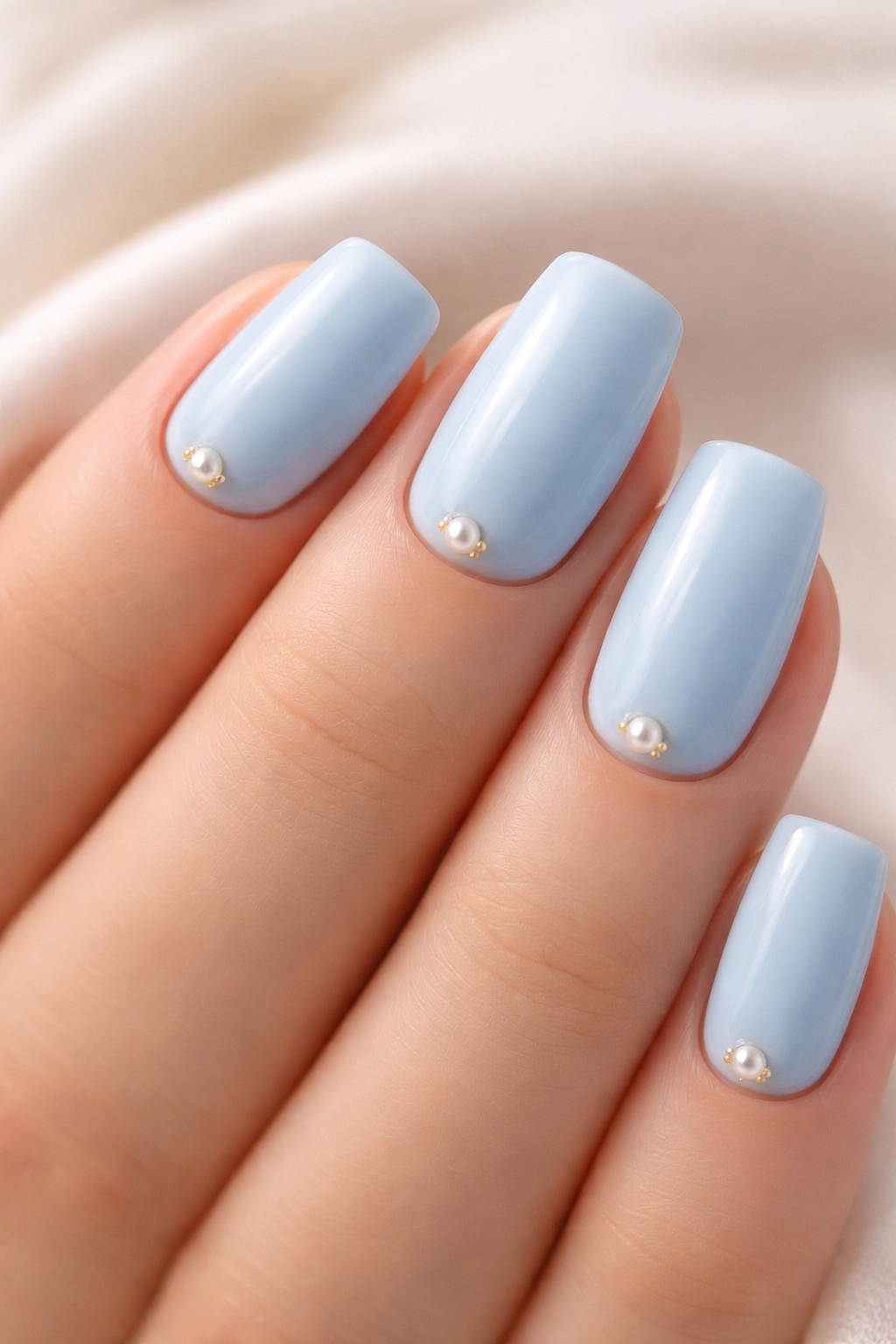 Nails with baby blue polish and tiny pearl accents near the cuticles.