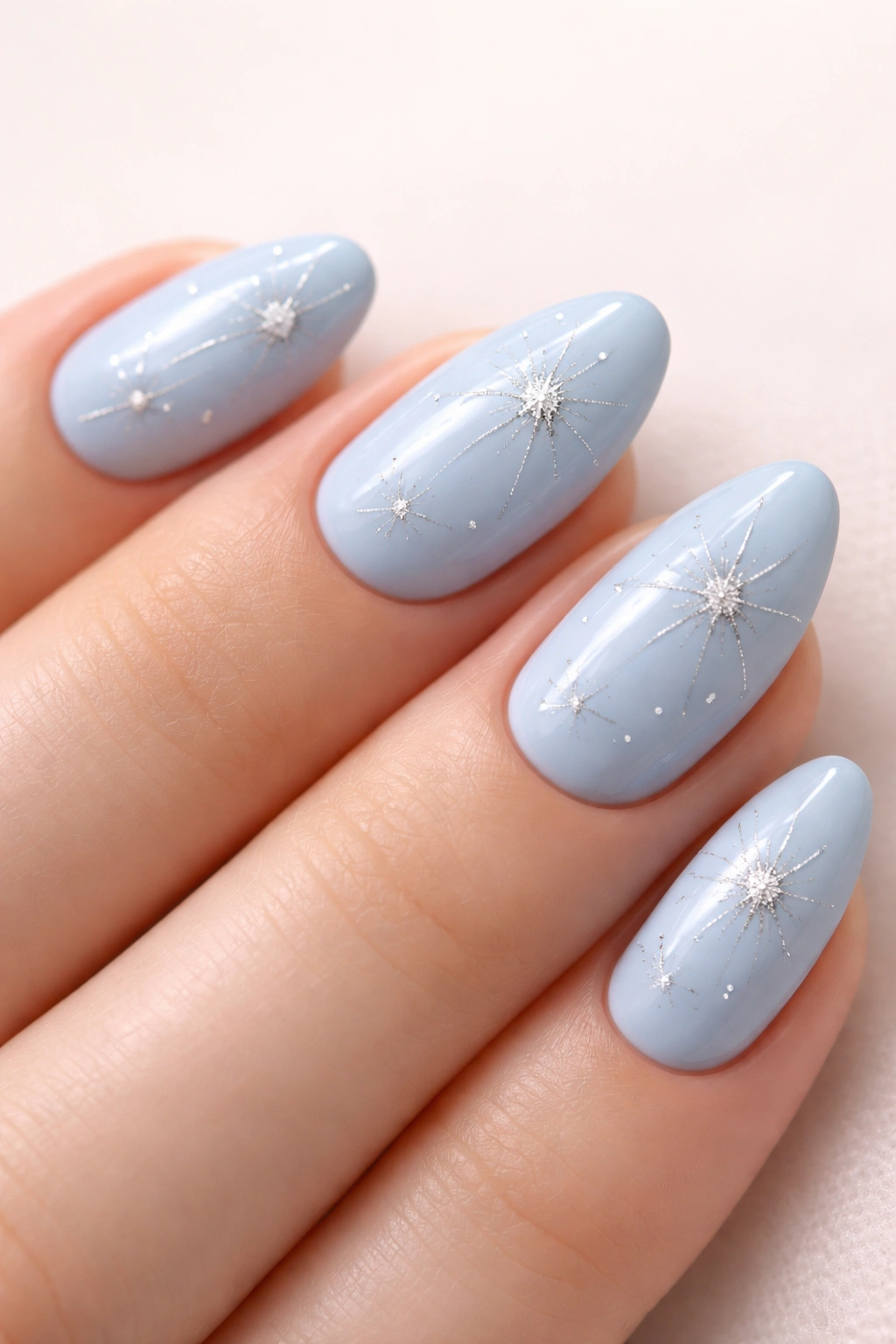 Baby blue almond nails with silver starbursts on pale background