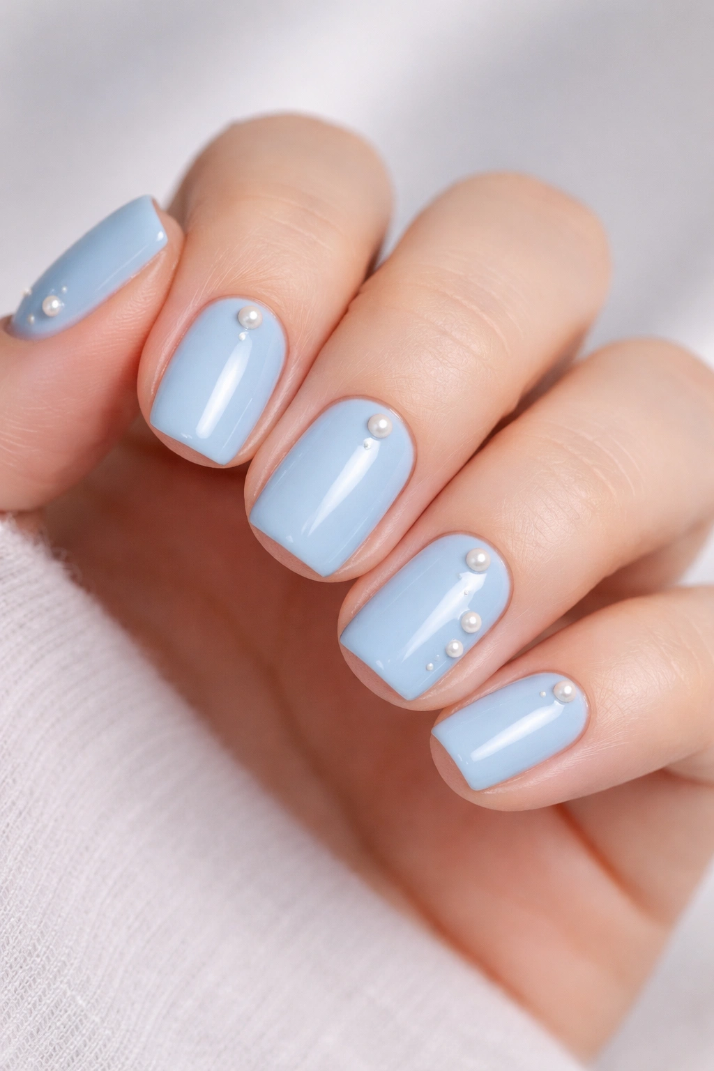 Close-up of short squoval nails in glossy baby blue with pearl accents