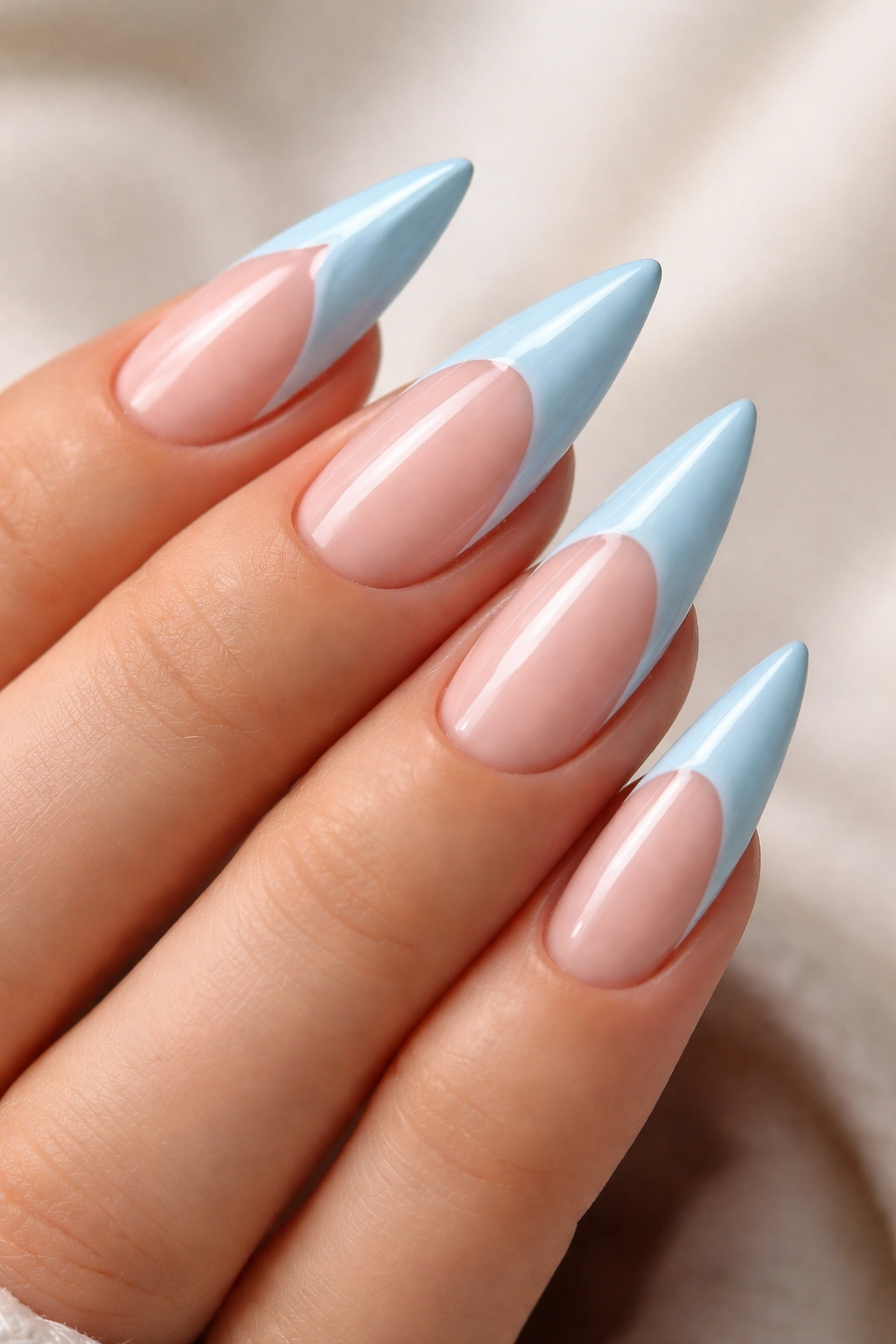 Stiletto nails featuring a nude base with baby blue reverse French tips