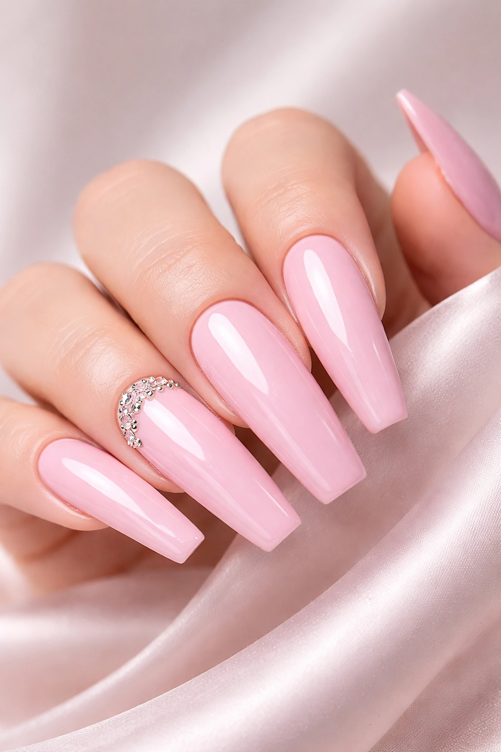 Close-up of baby pink acrylic nails with a glossy finish and a rhinestone accent