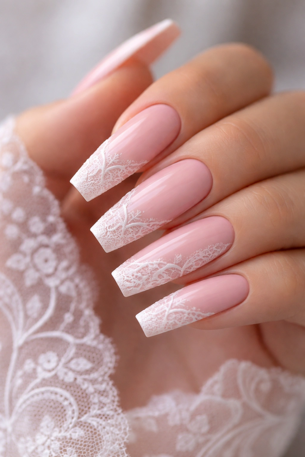 Close-up of baby pink coffin nails with delicate white lace patterns