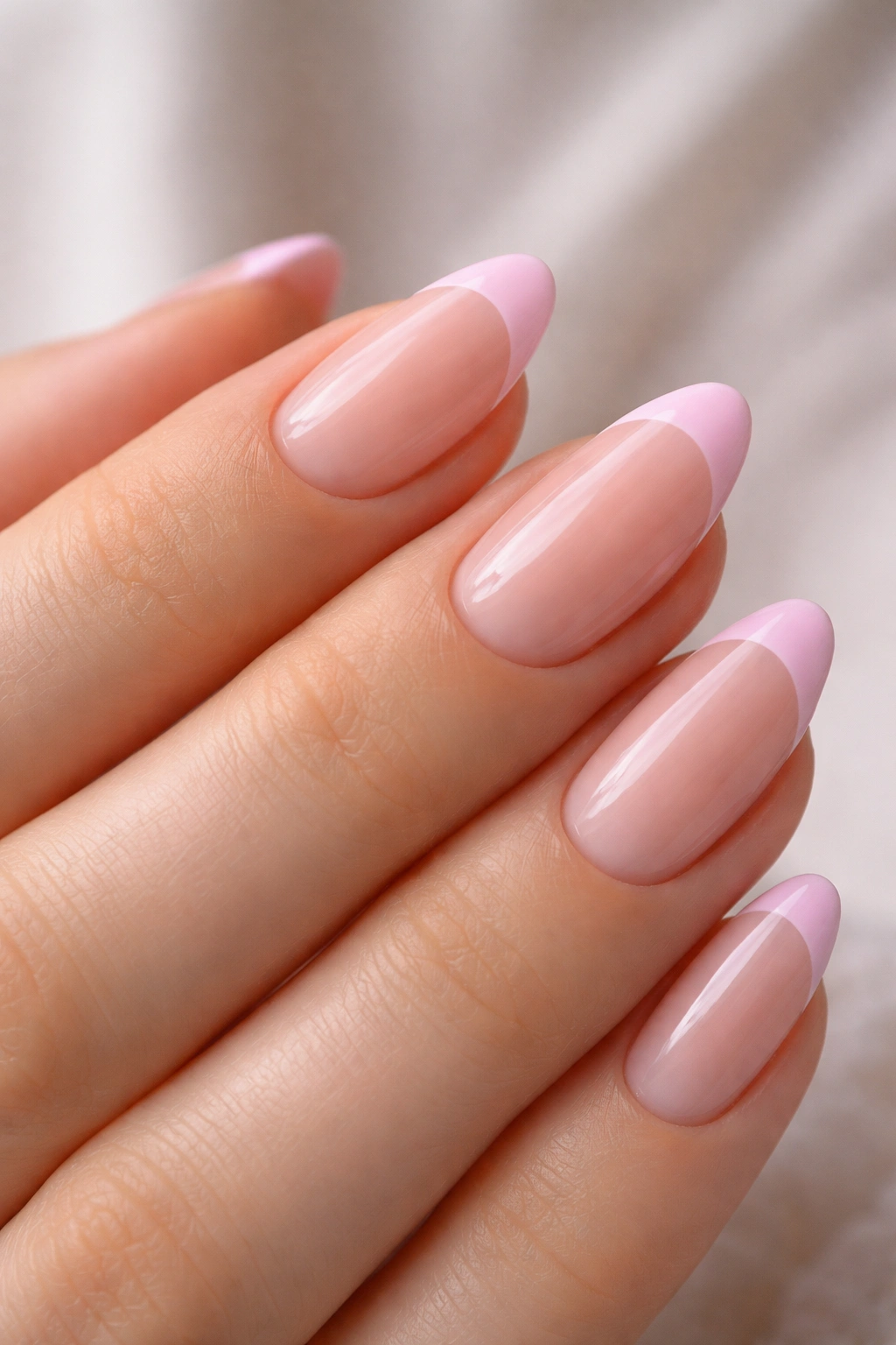 Close-up of short almond nails with baby pink French tips on a neutral background