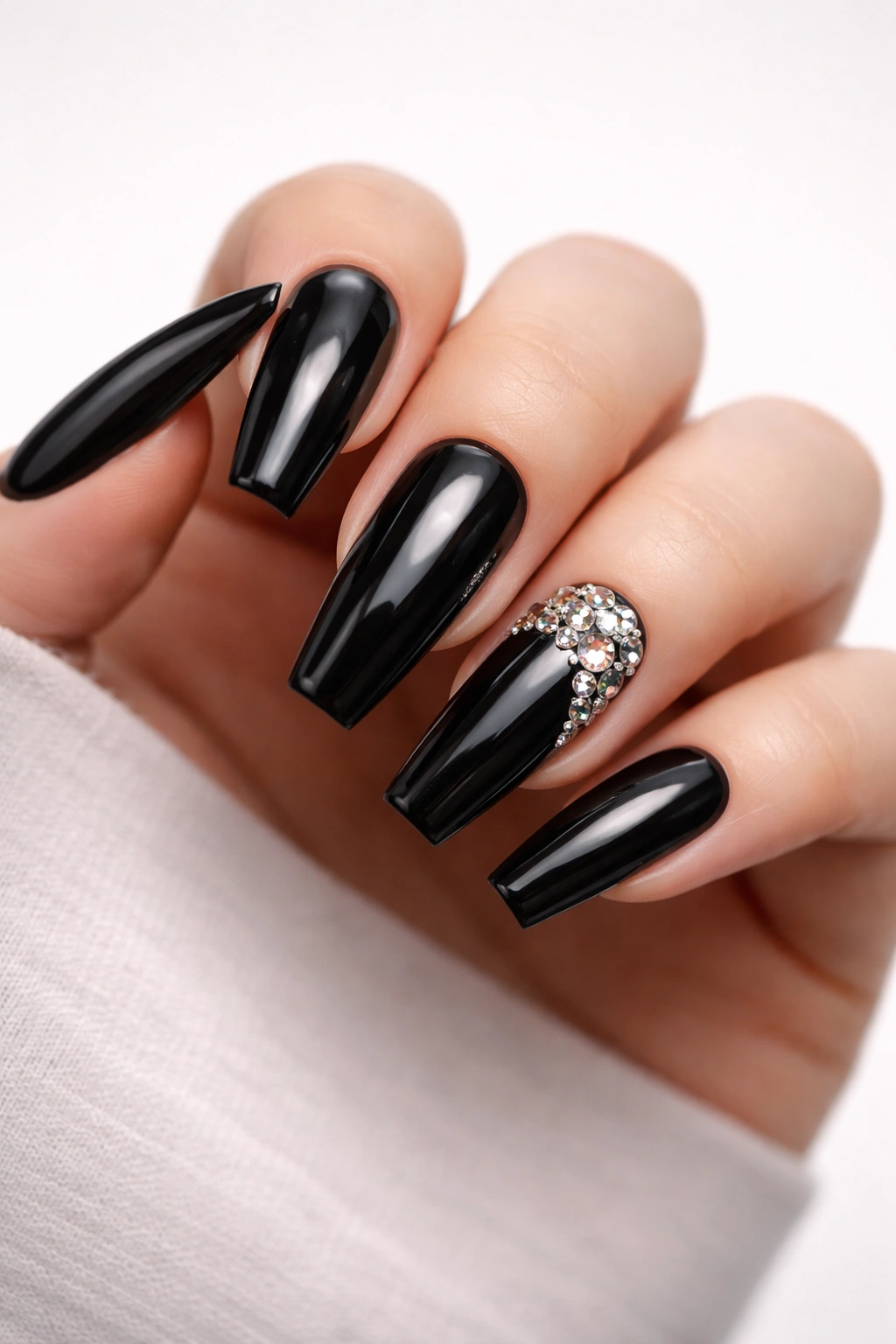Close-up of glossy black coffin nails with rhinestones on a hand, baddie nail art