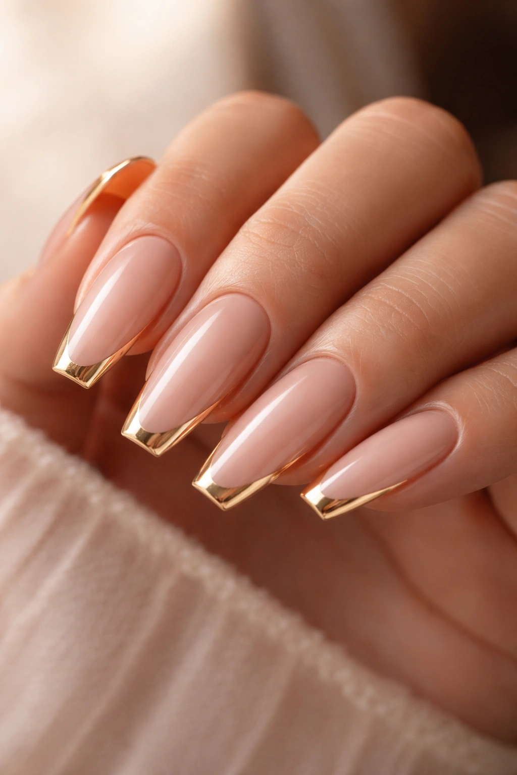 Close-up of nude ballerina nails with a fine gold edge on the flat tips.