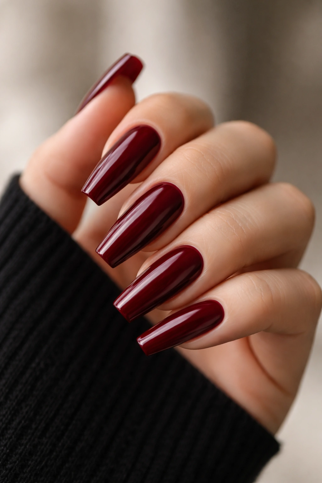 Close-up of dark red ballerina nails with tapered tips on a nude hand