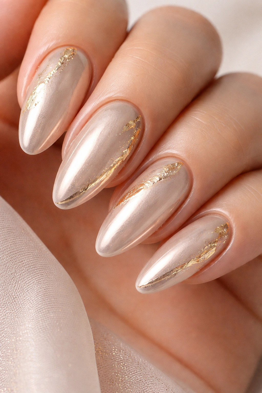 Close-up of beige chrome nails with gold foil accents.