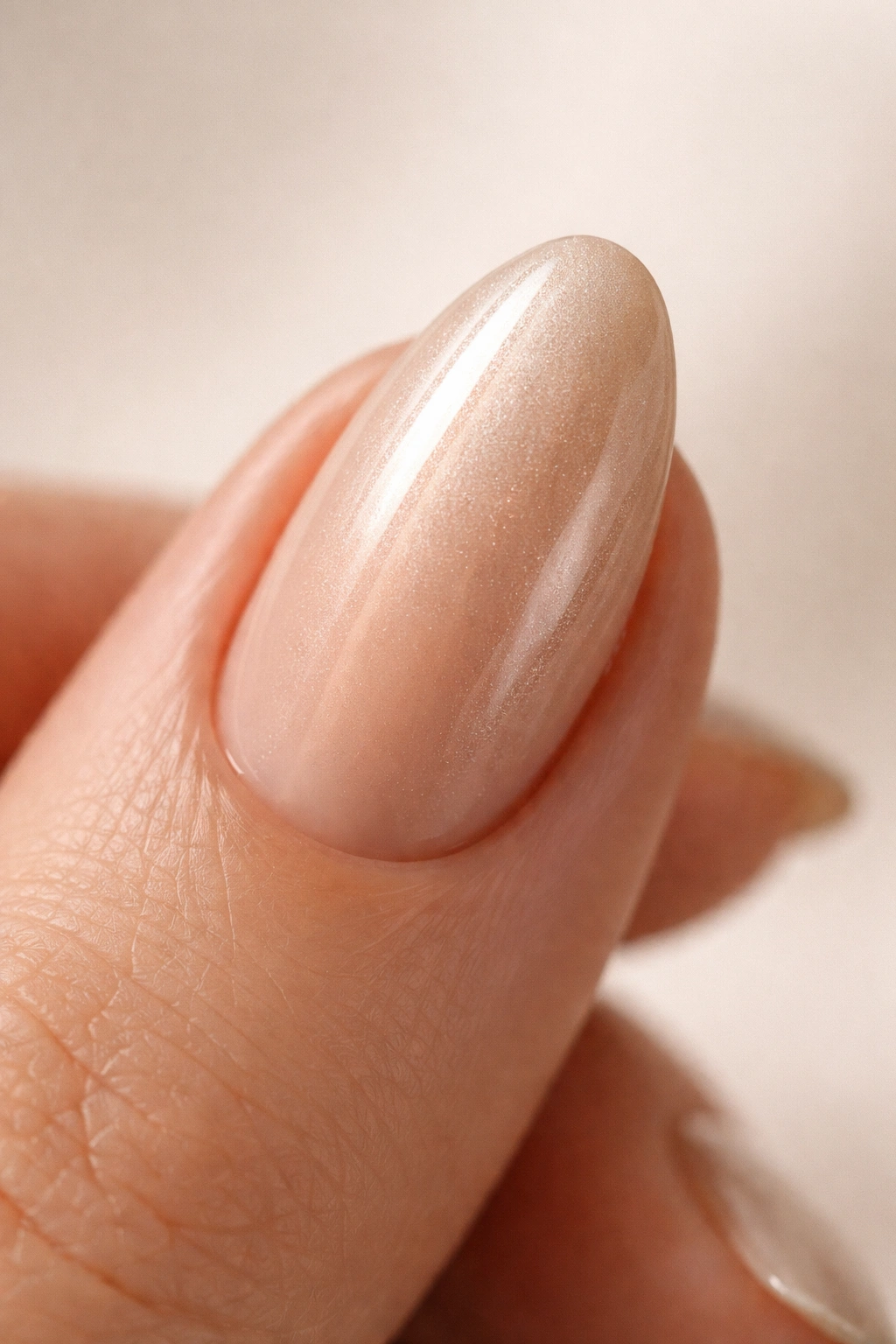 Close-up of a short almond nail with beige chrome glaze over nude base