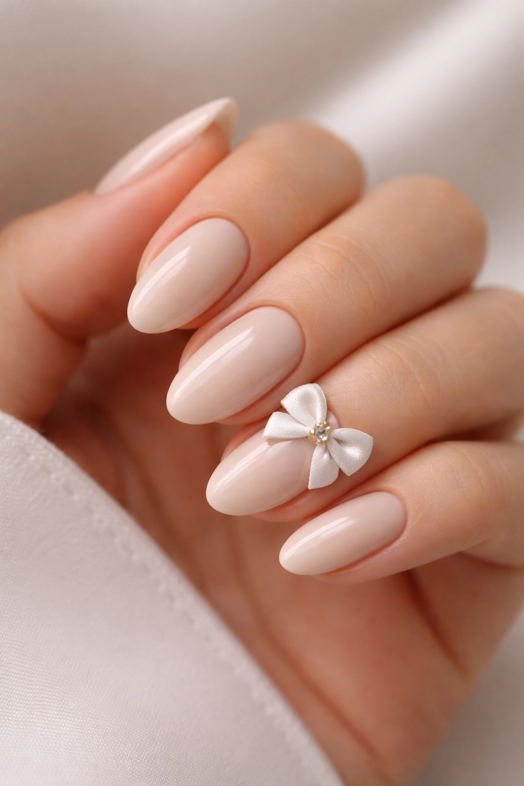 Beige almond nails with a single large bow on the accent nail