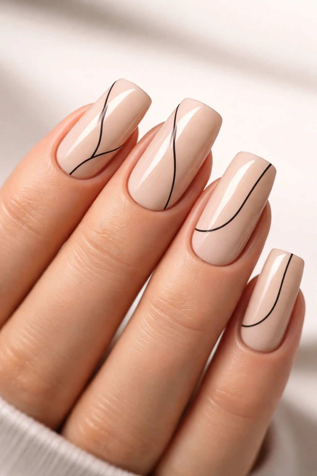 Close-up of warm beige nails with black line details and negative space on soft square nails