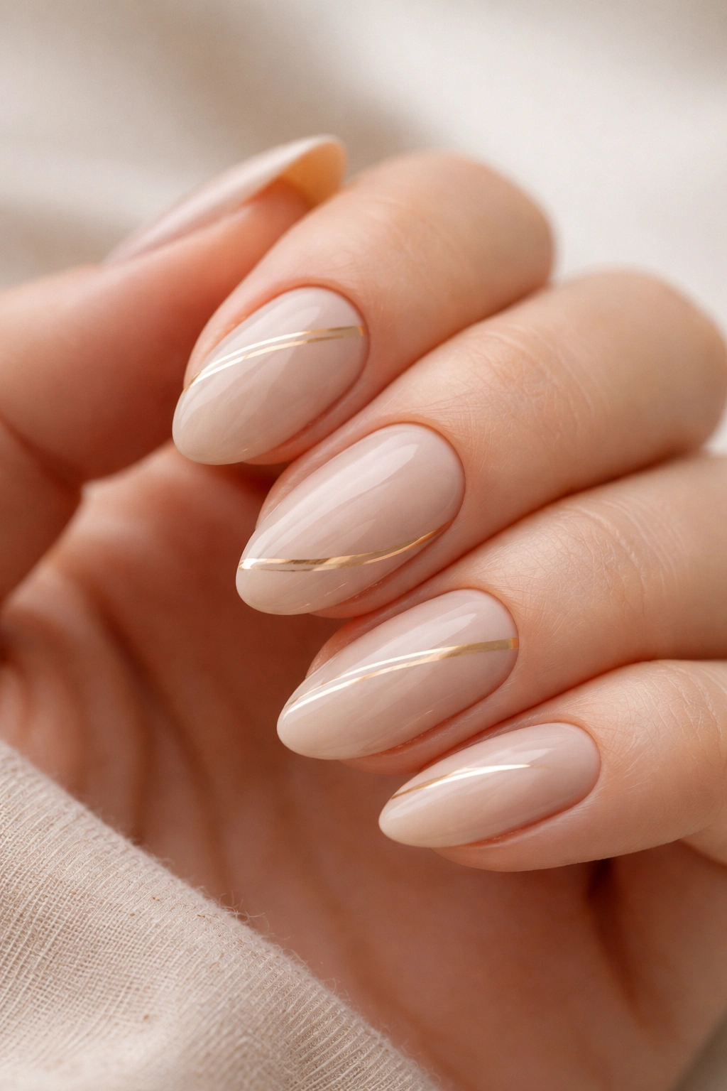 Close-up of beige almond nails with ultra-thin gold lines