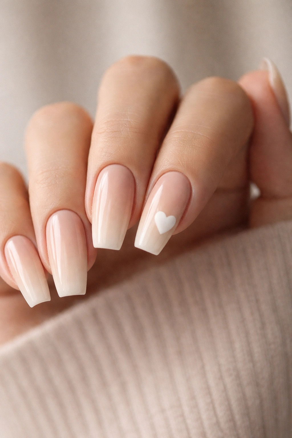Beige ombre nails with a single white heart accent