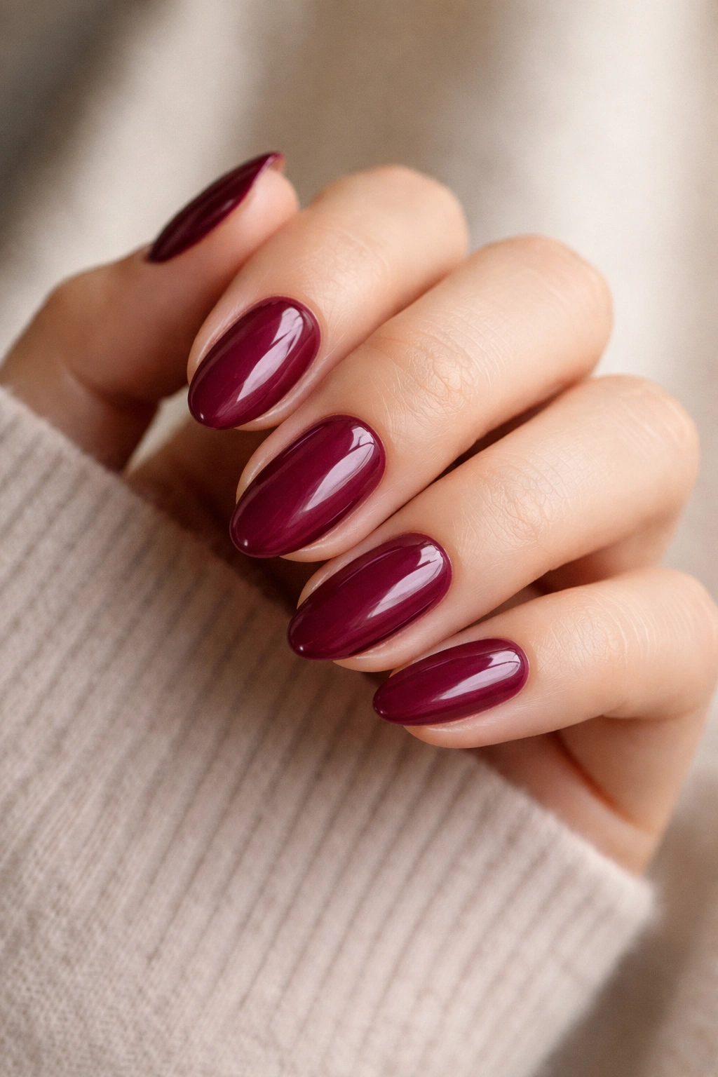 Close-up of short almond nails painted in berry shade with glossy finish