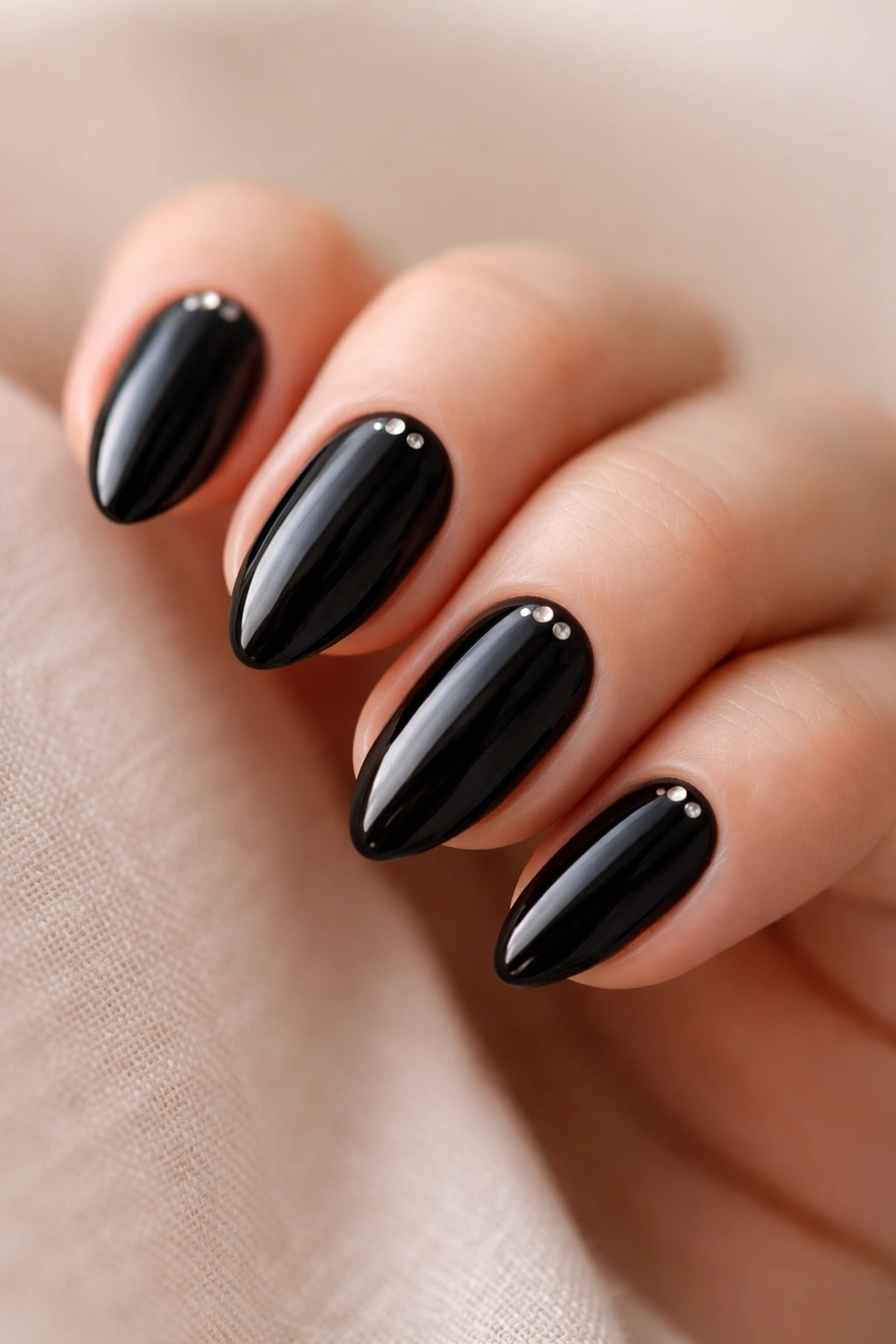 Close-up of black almond nails with tiny silver dots near the cuticles