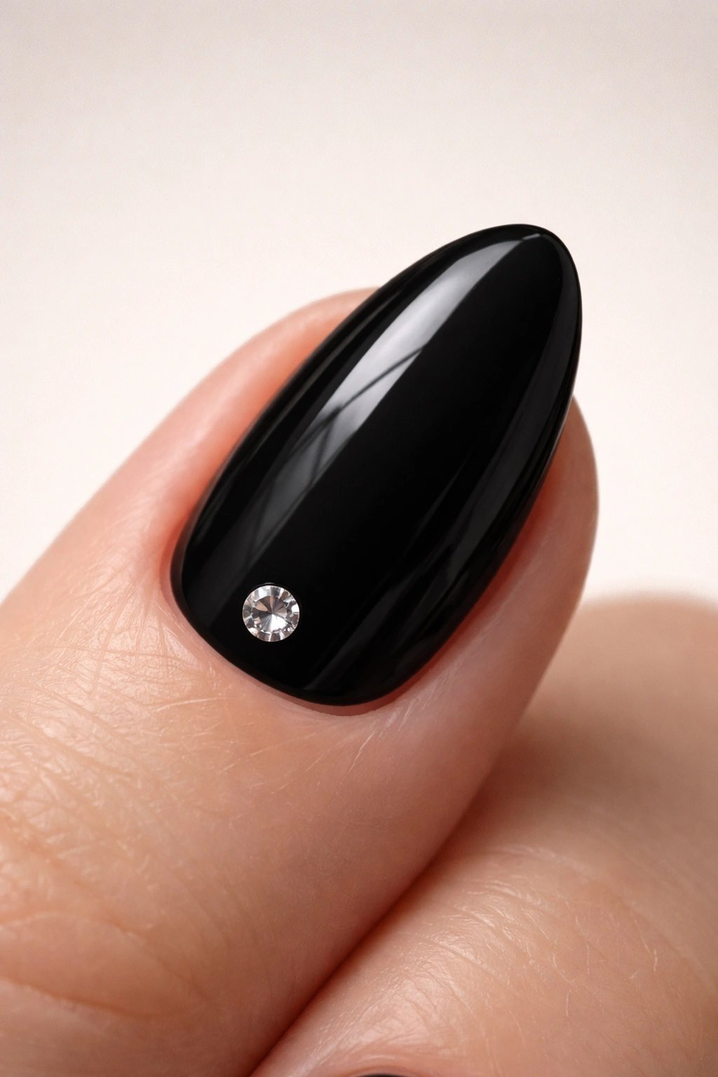 Close-up of a black almond nail with a single glossy gem near the base