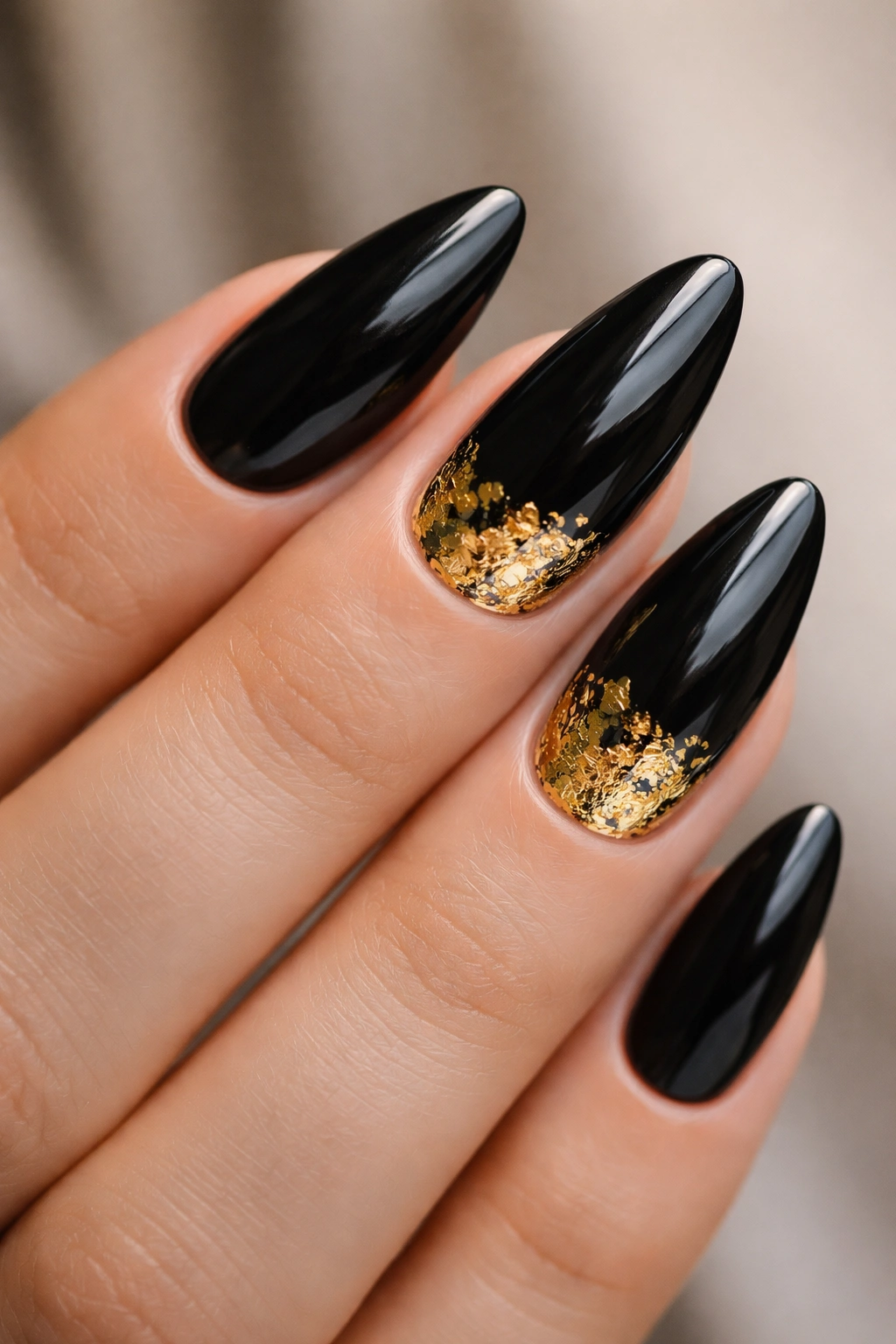 Close-up of black almond nails with irregular gold foil accents
