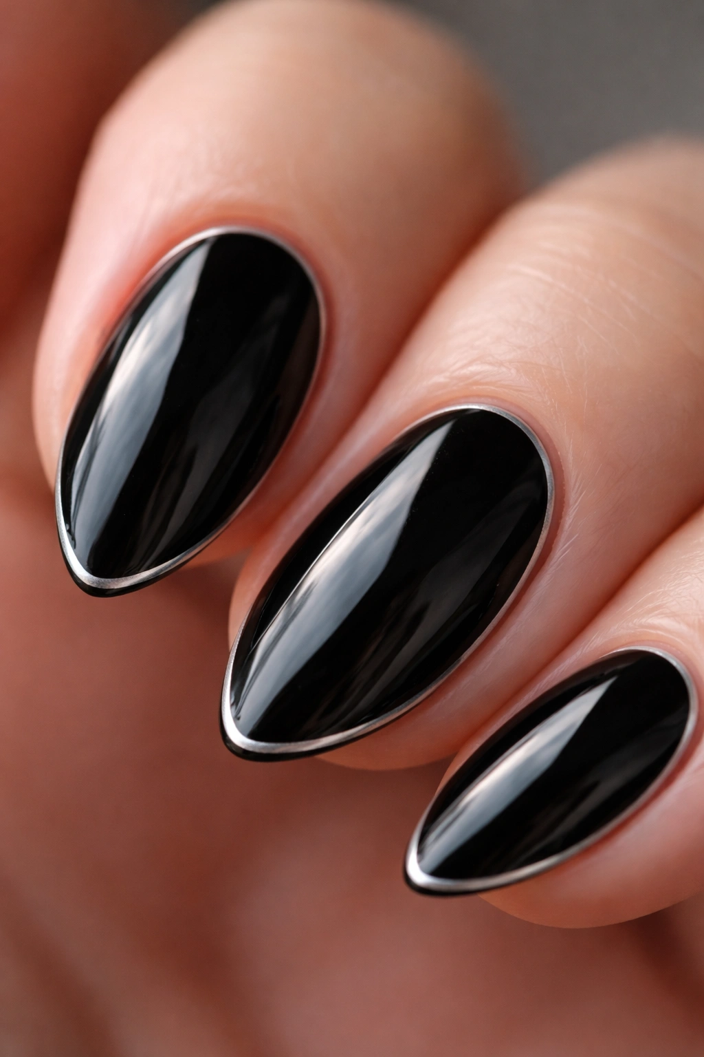 Close-up of a short black almond nail with a thin silver outline