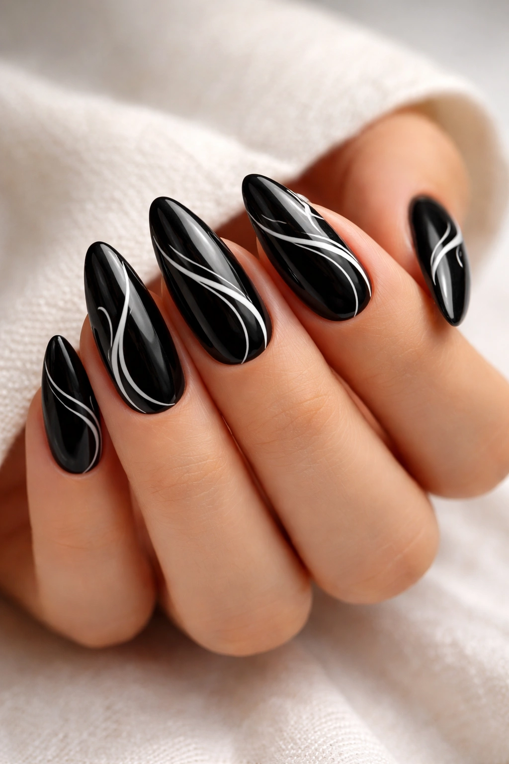 Close-up of black almond nails with white swirling nail art