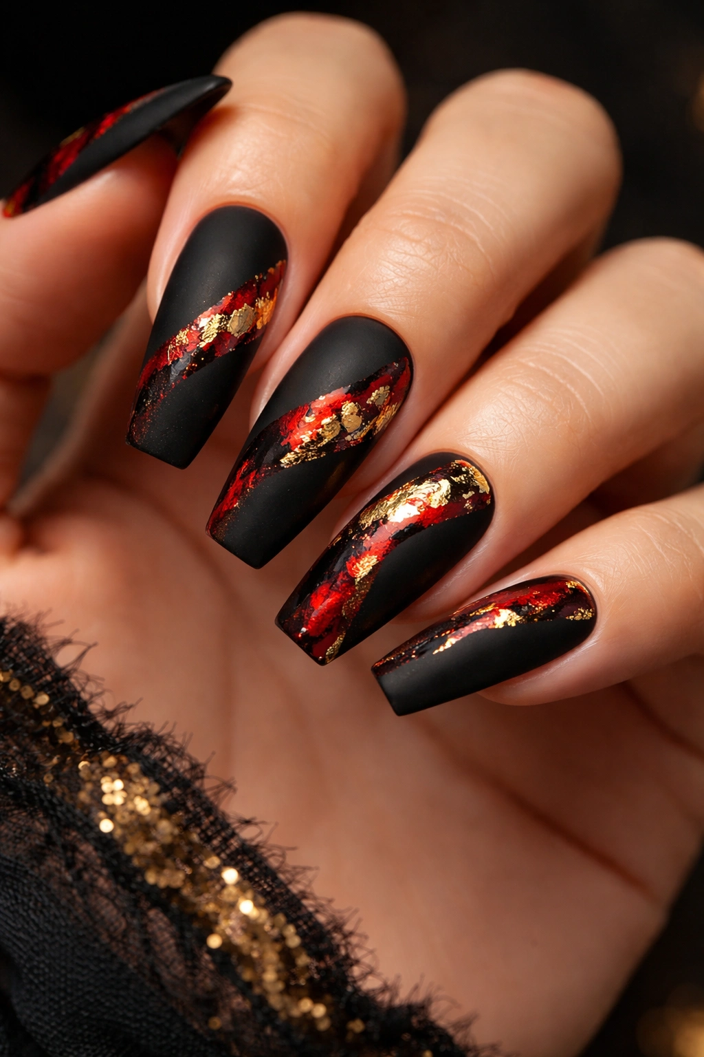 Matte black coffin nails with red accents and gold foil details catching light