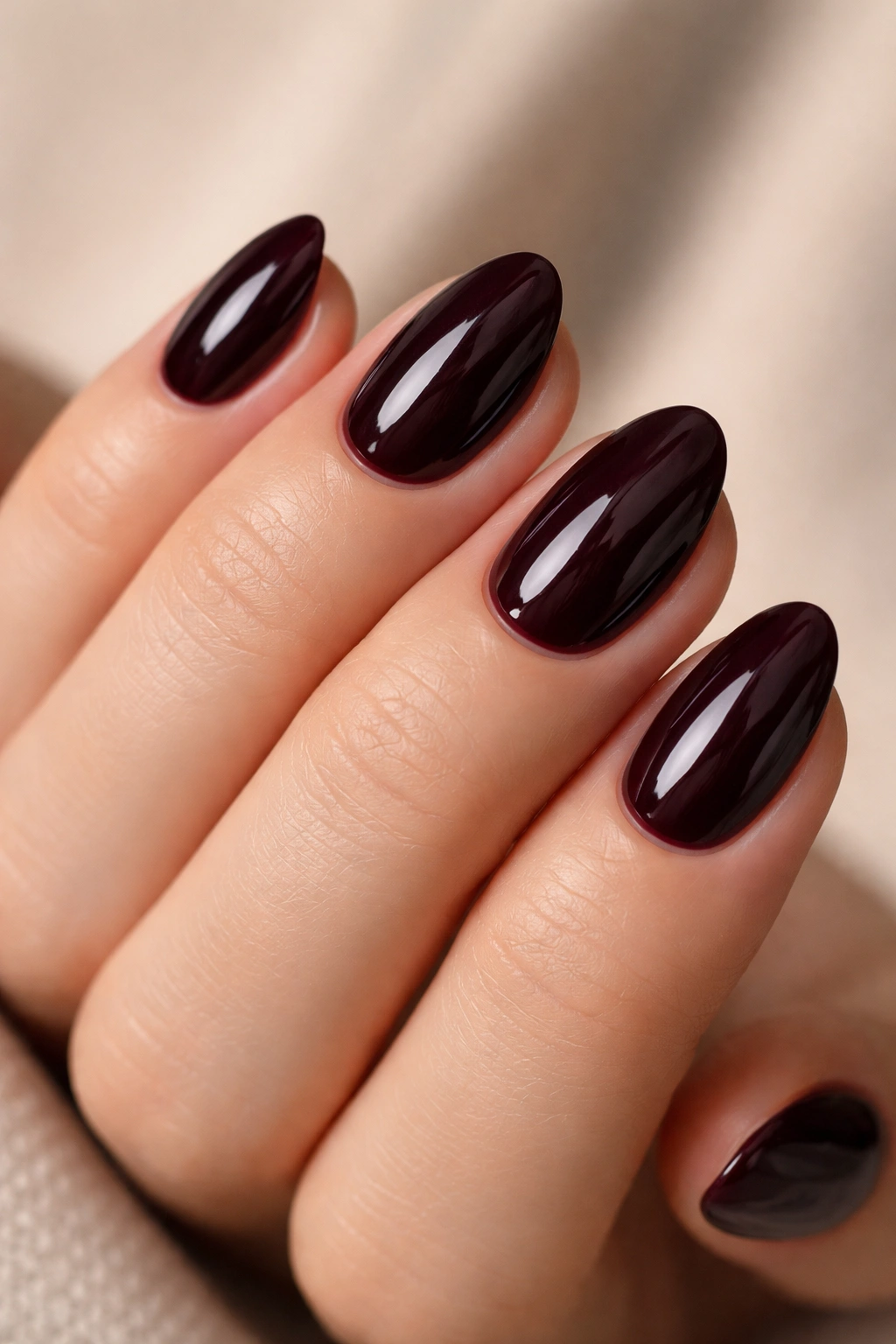 Close-up of black cherry short almond nails on a bare hand