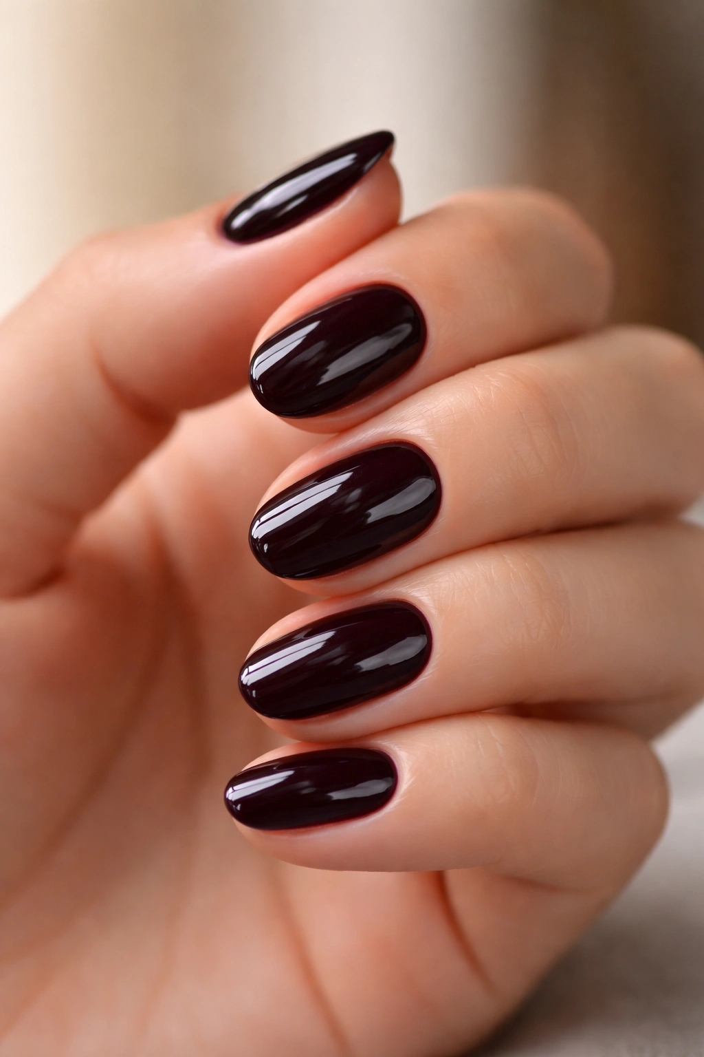 Close-up of short oval nails in deep black cherry polish with high shine