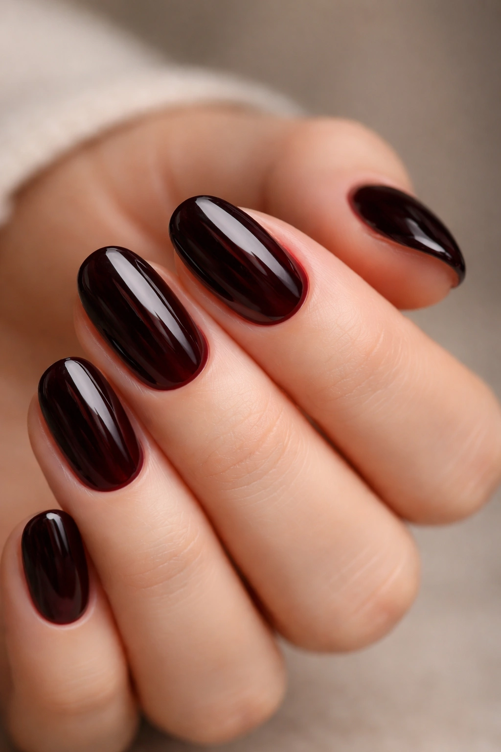 Close-up of glossy black cherry short oval nails on hand with neutral background