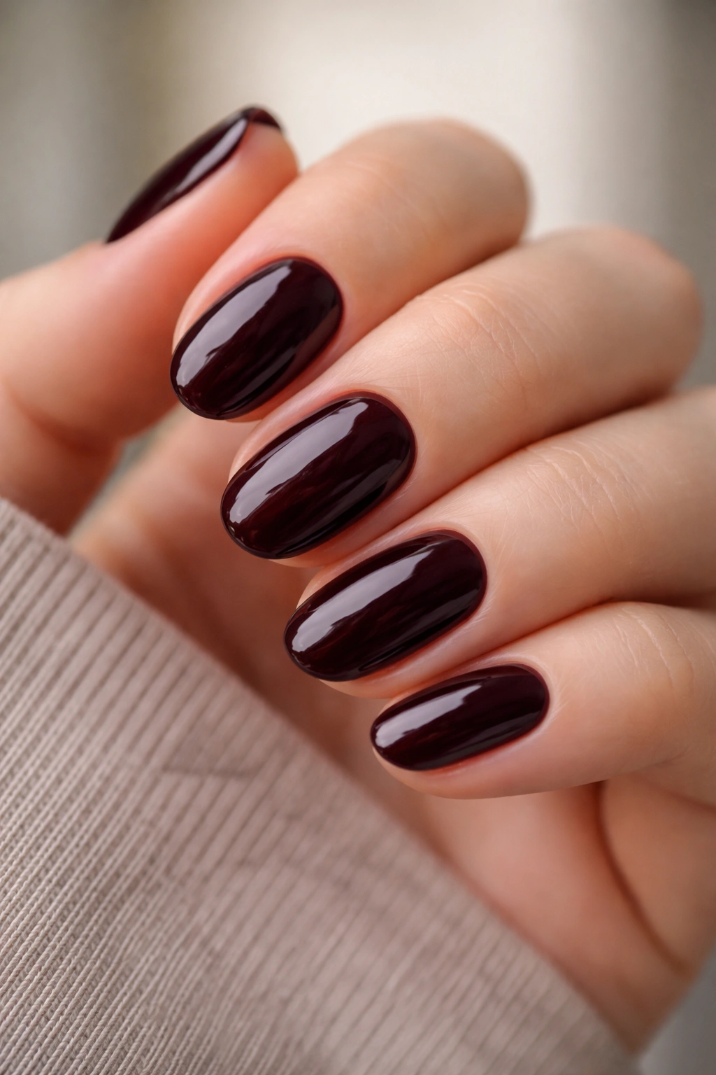Close-up of short oval nails painted deep wine plum with glossy finish