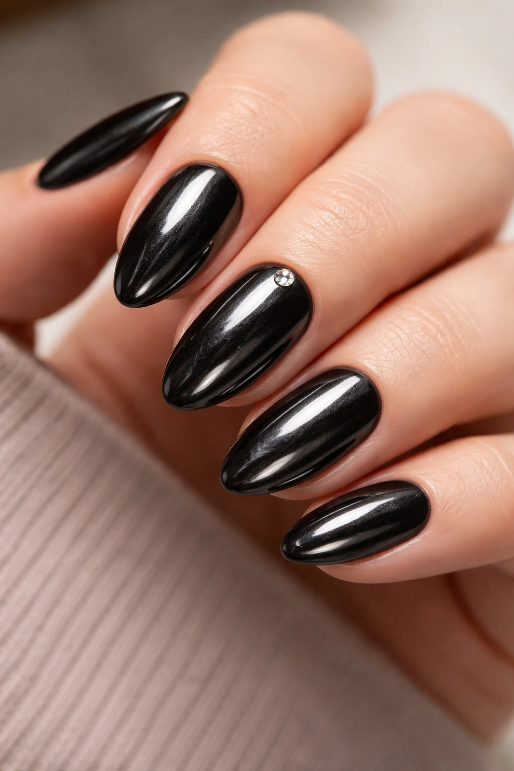 Close-up of short almond nails in black chrome with a micro rhinestone at the base