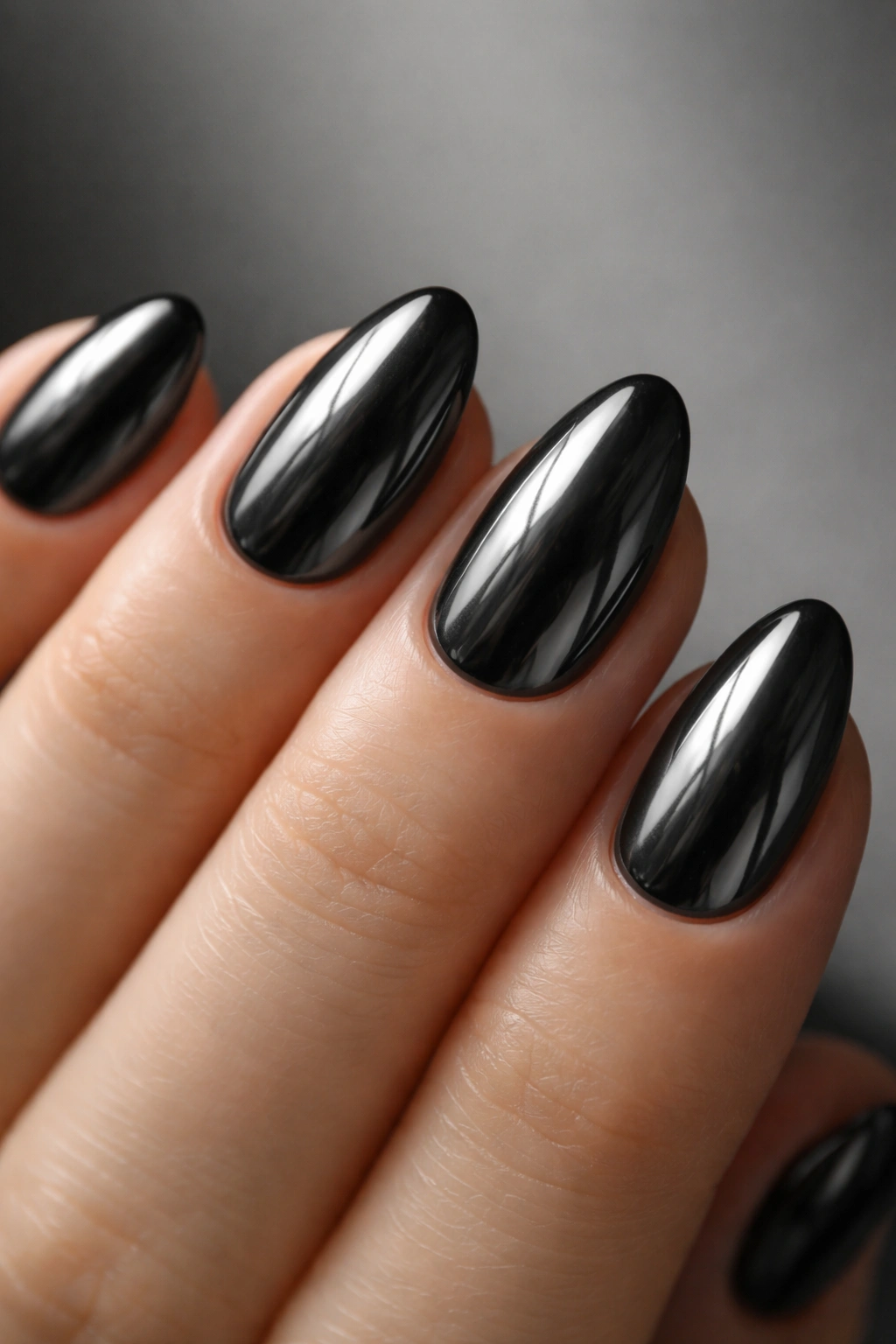 Close-up of a hand with tiny short almond nails in black chrome with graphite sheen.
