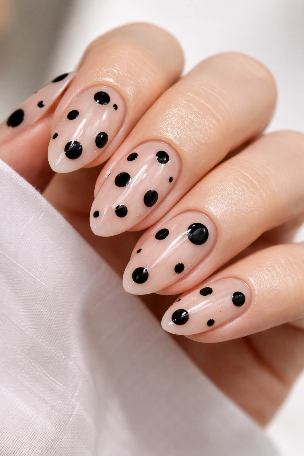Black dots on sheer nude nails with a glossy finish on short almond nails