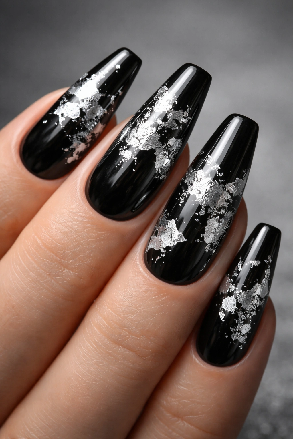 Close-up of black nails with silver foil accents creating a metallic abstract pattern