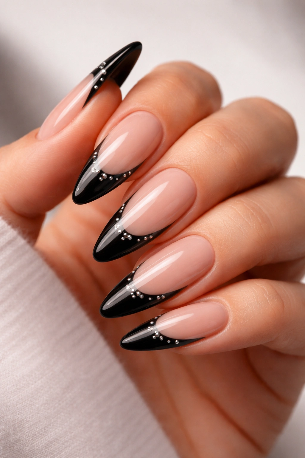 Close-up of nails with black tips and subtle studs on nude base.