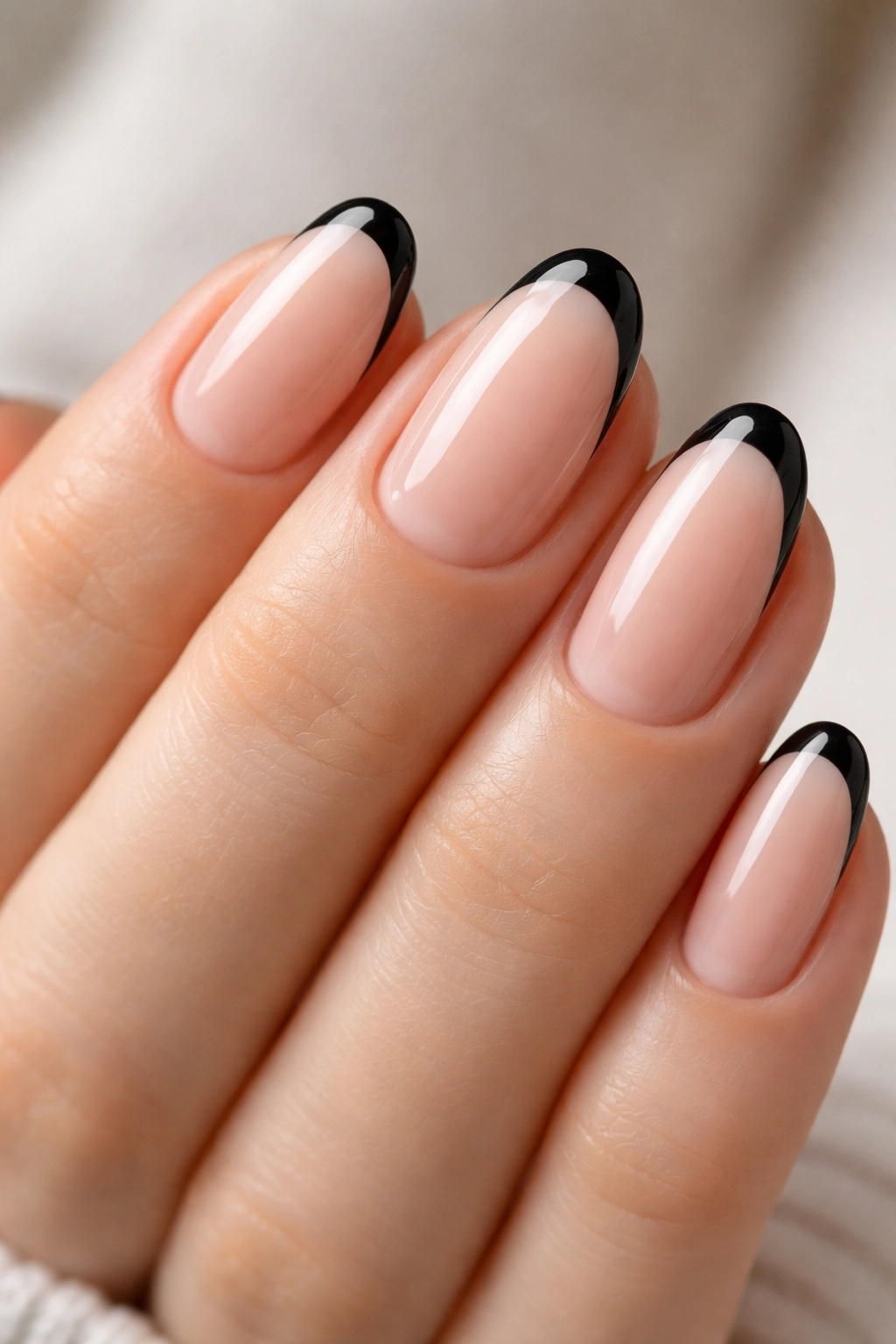 Short oval nails with sheer nude base and slim black French tips