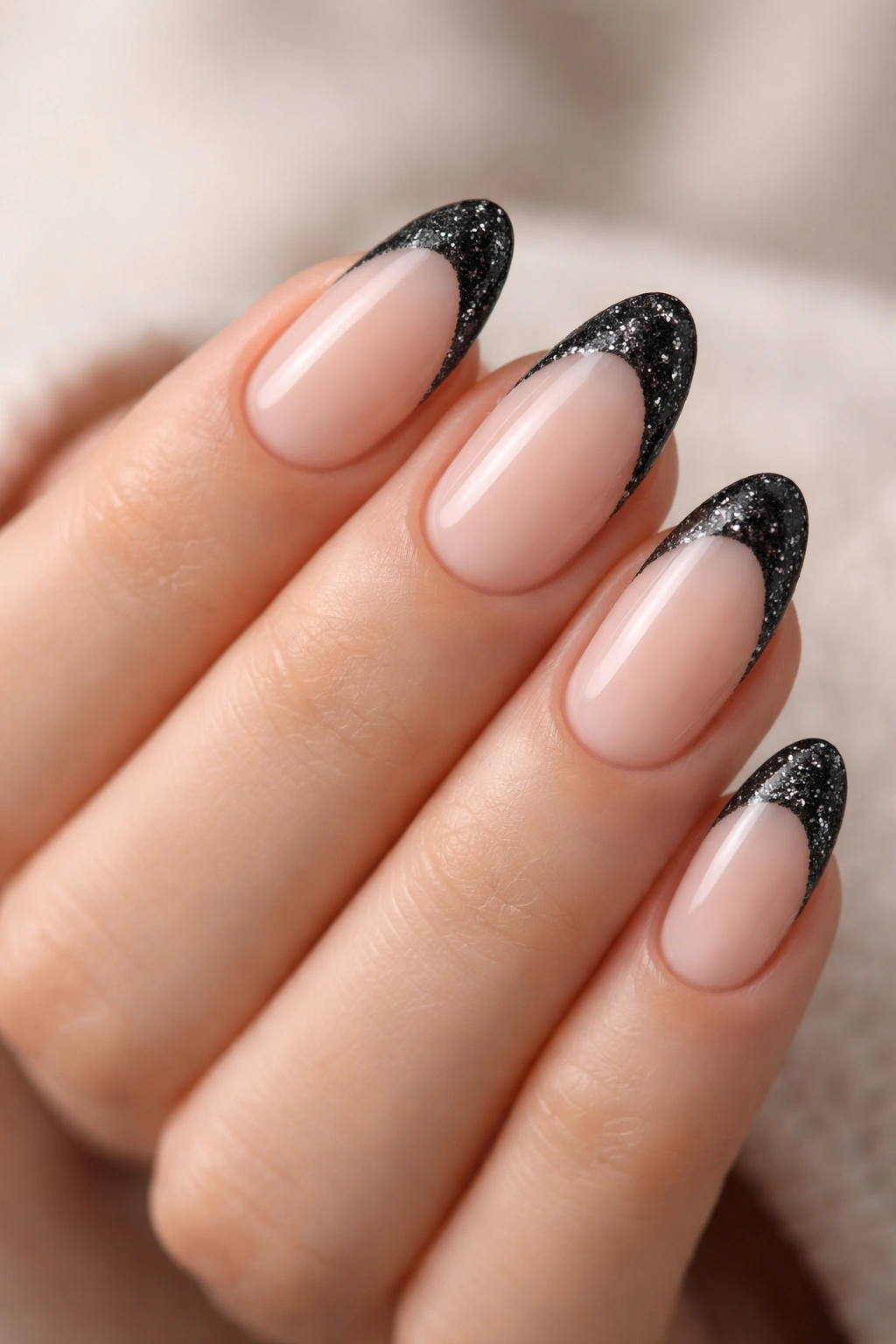 Close-up of short almond nails with black glitter French tips on nude base