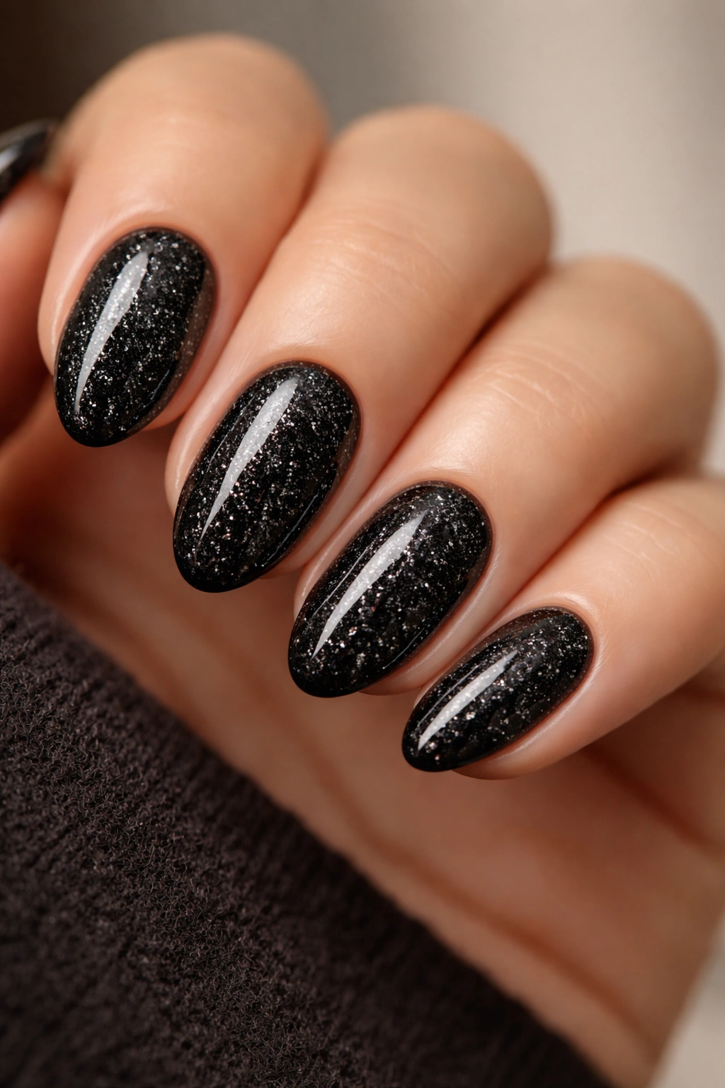 Close-up of short almond nails with black glitter on jet-black polish