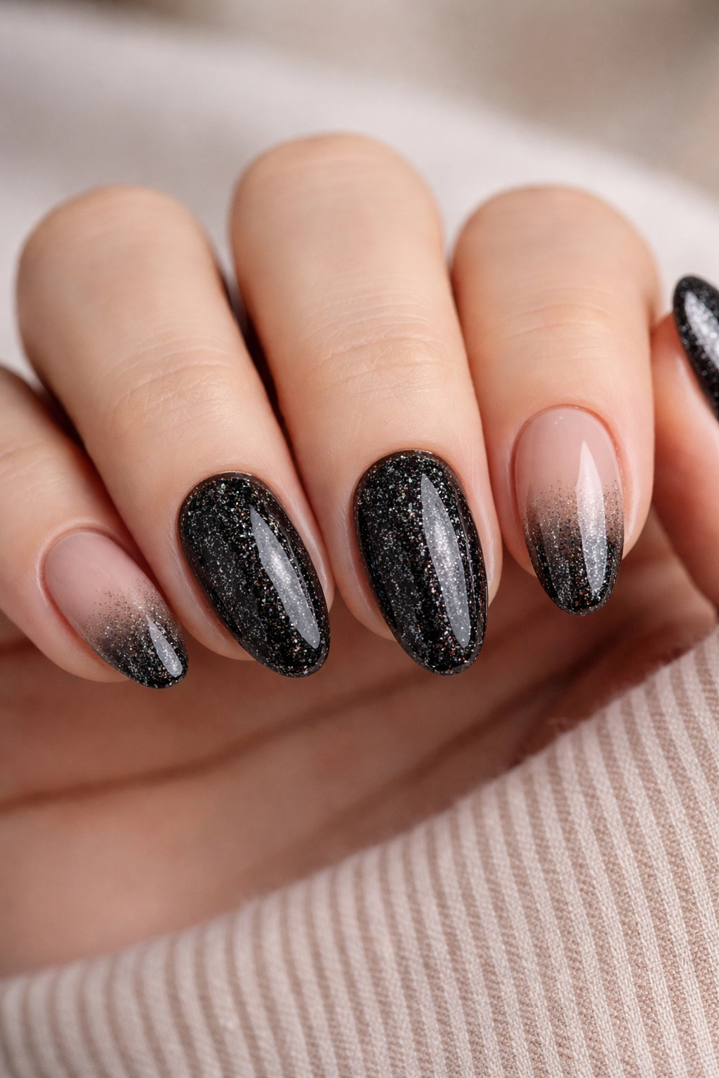 Close-up of short almond nails with nude bases and black glitter accents