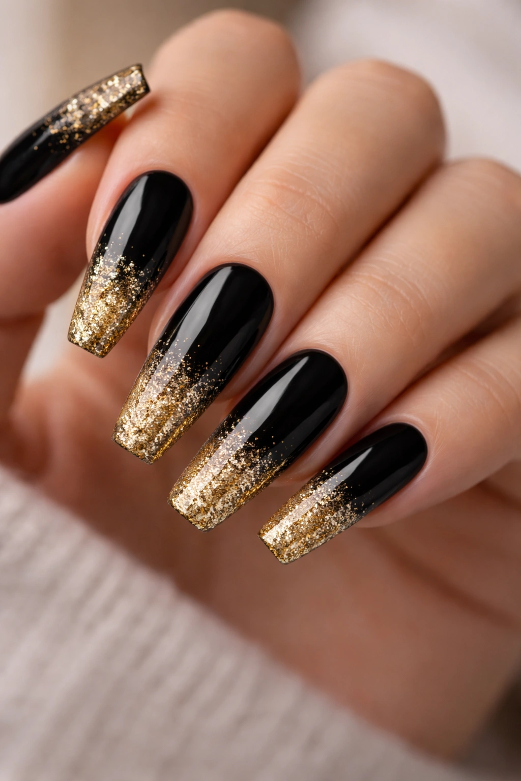 Close-up of black coffin nail with gold glitter tips and gradient shimmer