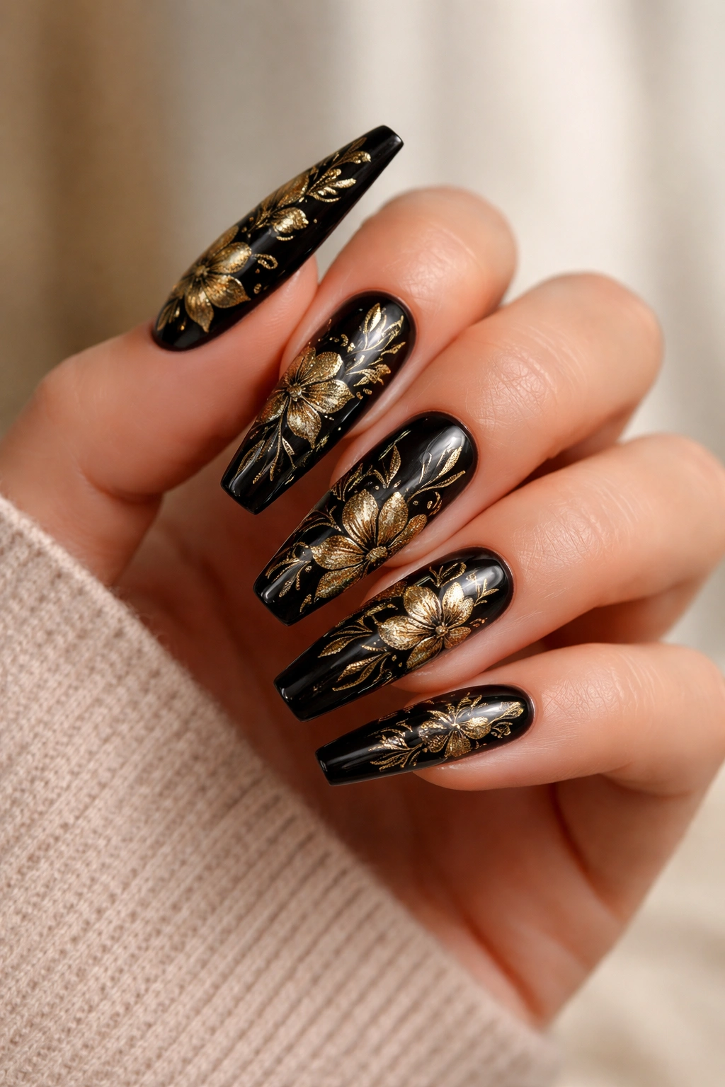 Black coffin nails with delicate gold floral patterns on a neutral background