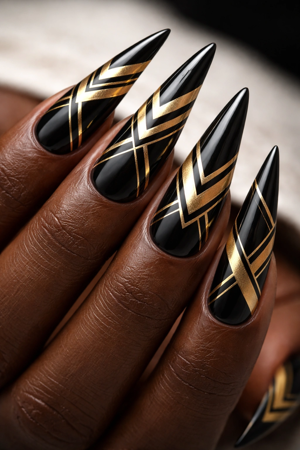 Stiletto nails with black and gold geometric patterns and sharp lines.
