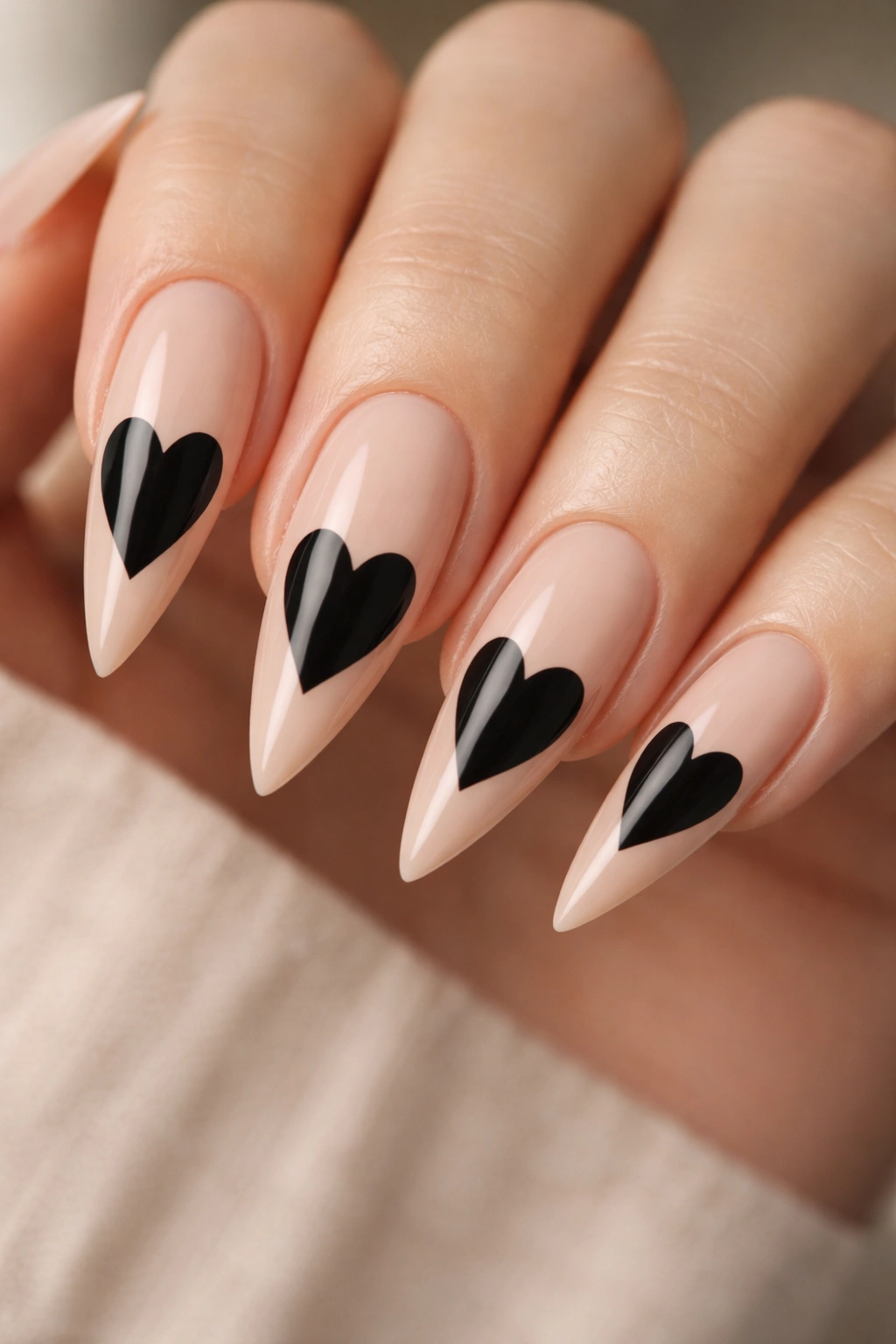 Nude-based stiletto nails featuring a bold black heart as the focal point