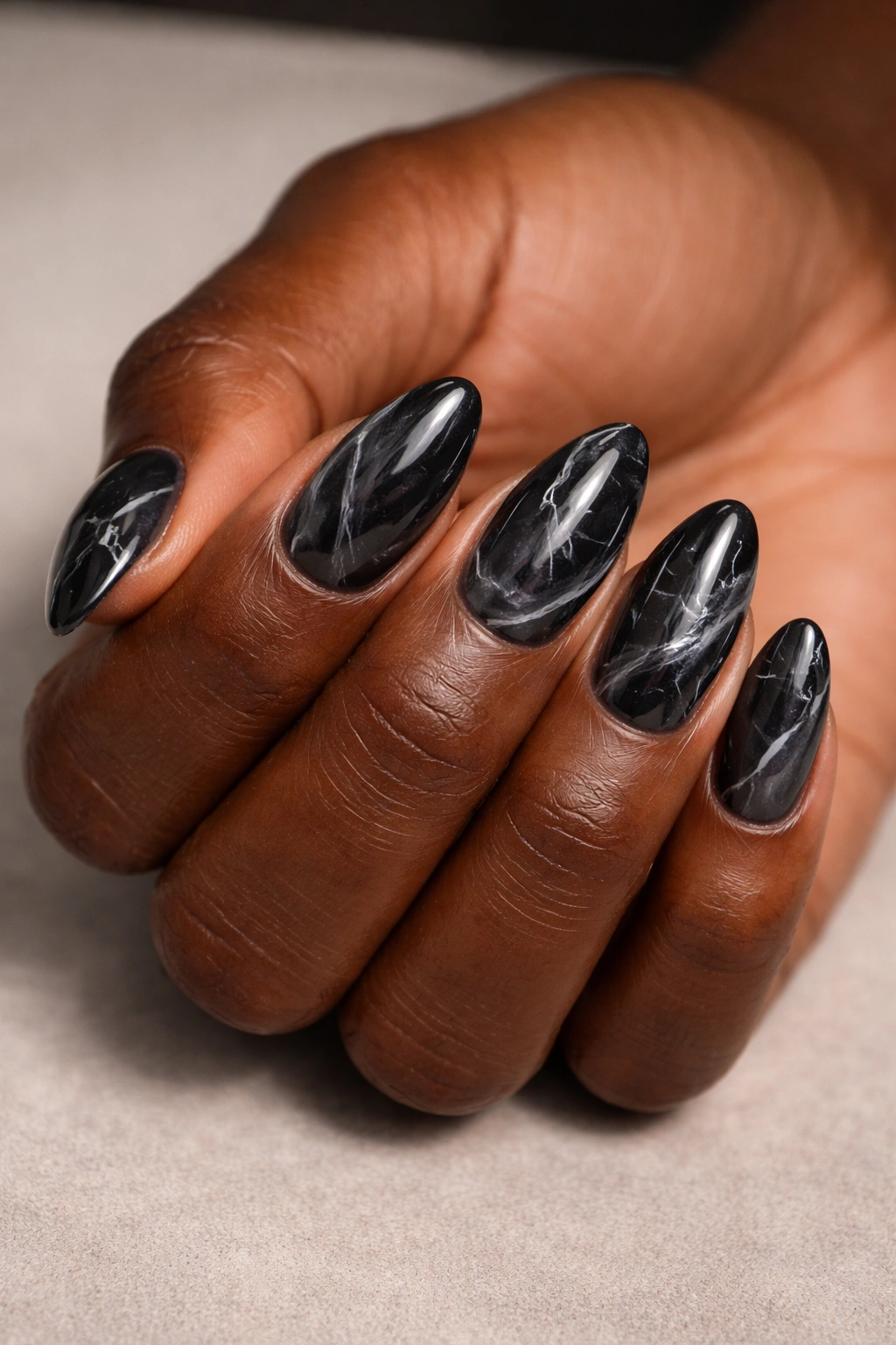 Close-up of short almond nails with translucent gray-black marble base and fine white veining