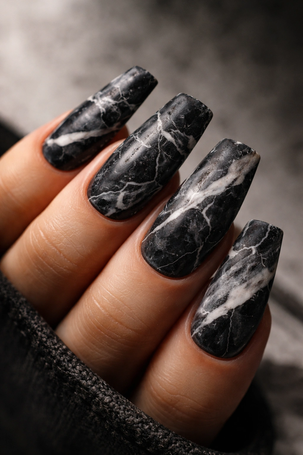 Close-up of black nails with white and gray marble veining in a grunge matte finish