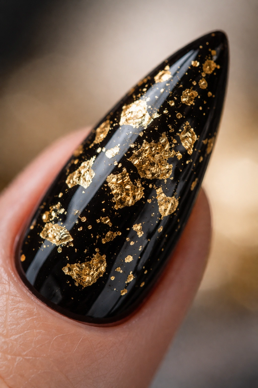 Close-up of a black stiletto nail with embedded gold foil flakes