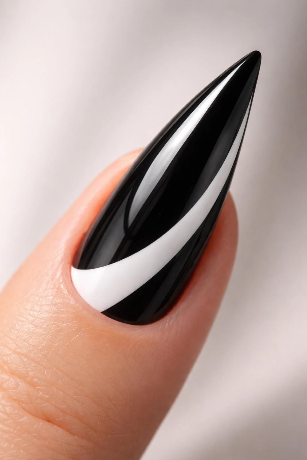 Glossy black curved stiletto nail with white negative-space French tip along the curve