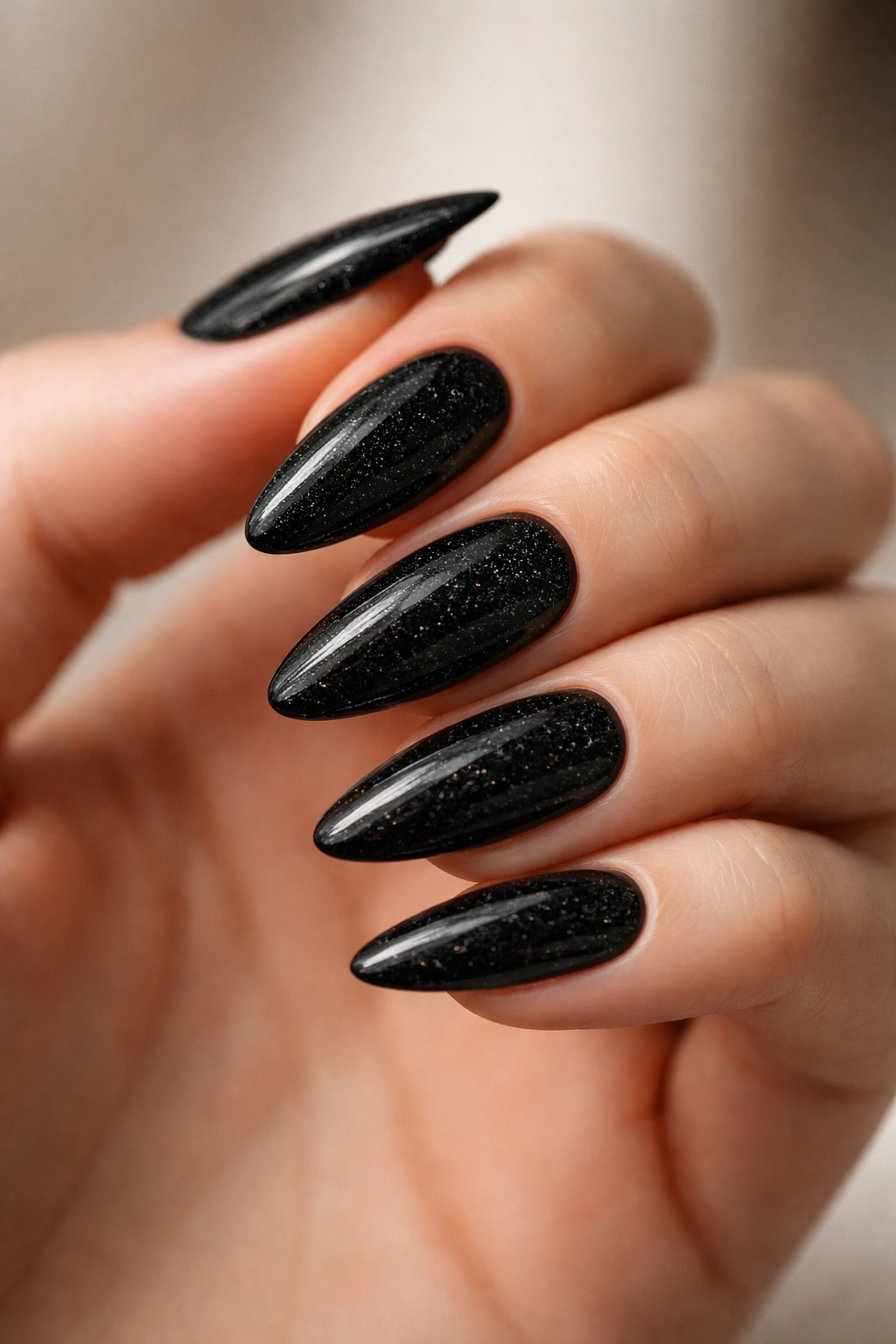 Close-up of glossy black almond nails with micro glitter on a neutral backdrop